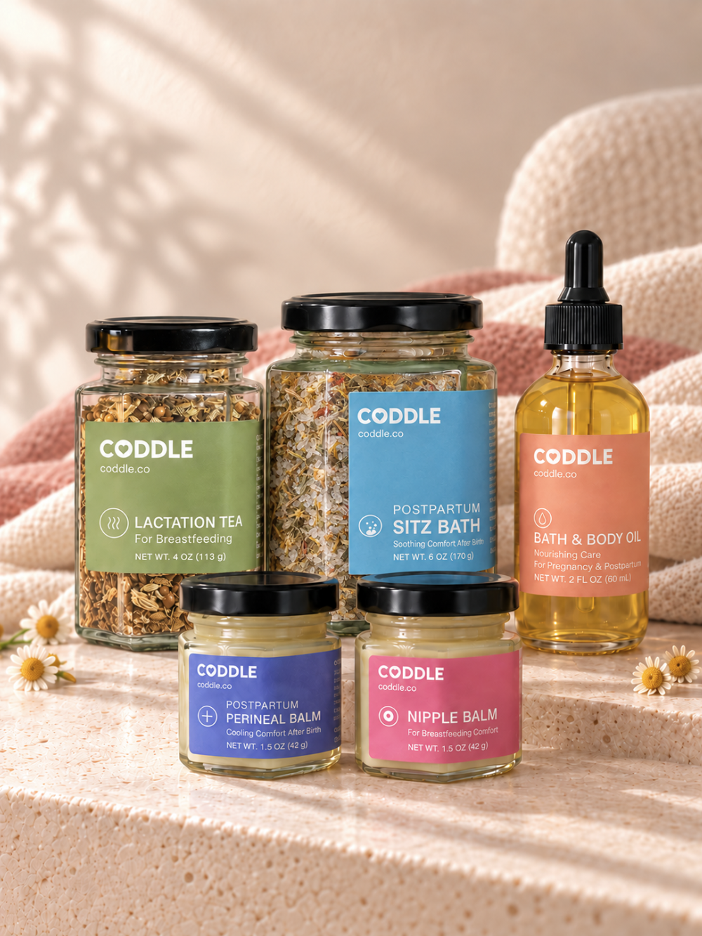 CODDLE postpartum recovery essentials arranged on soft white bedding.