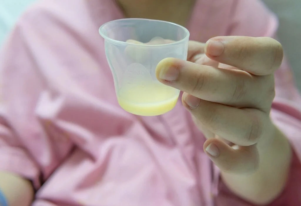 Mother holding a small cup of yellow colostrum breast milk after birth