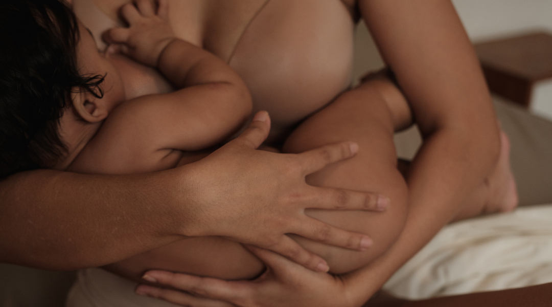 Mother breastfeeding her baby while supporting a tender breast affected by a clogged milk duct or mastitis.
