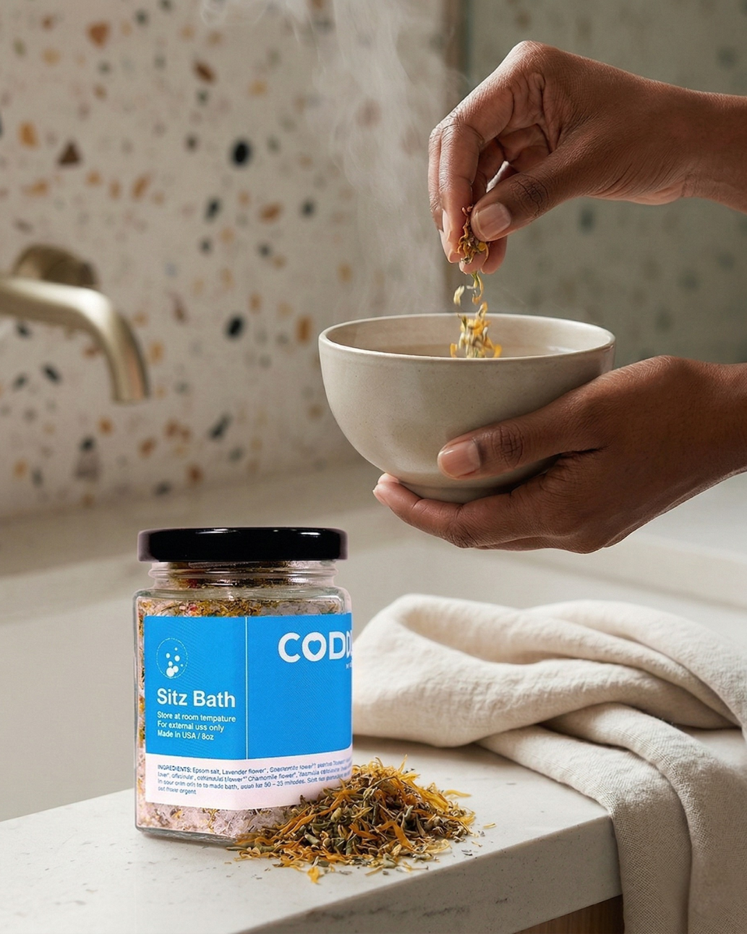 Hands adding herbal sitz bath soak into a bowl with steam, showing postpartum recovery use.