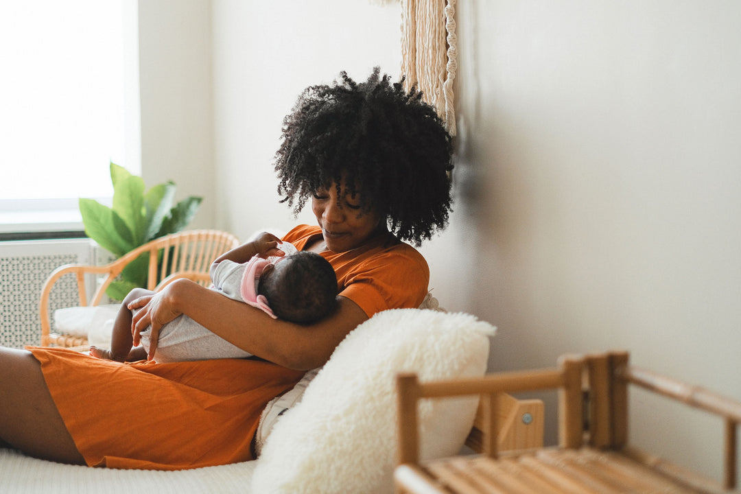 Black mother breastfeeding her newborn at home during the early postpartum period.