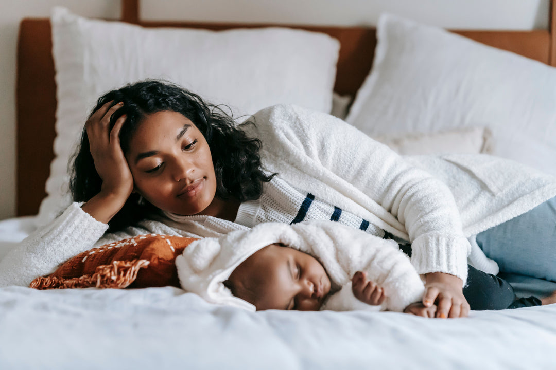 Mother lying beside her sleeping newborn during the early postpartum recovery period.