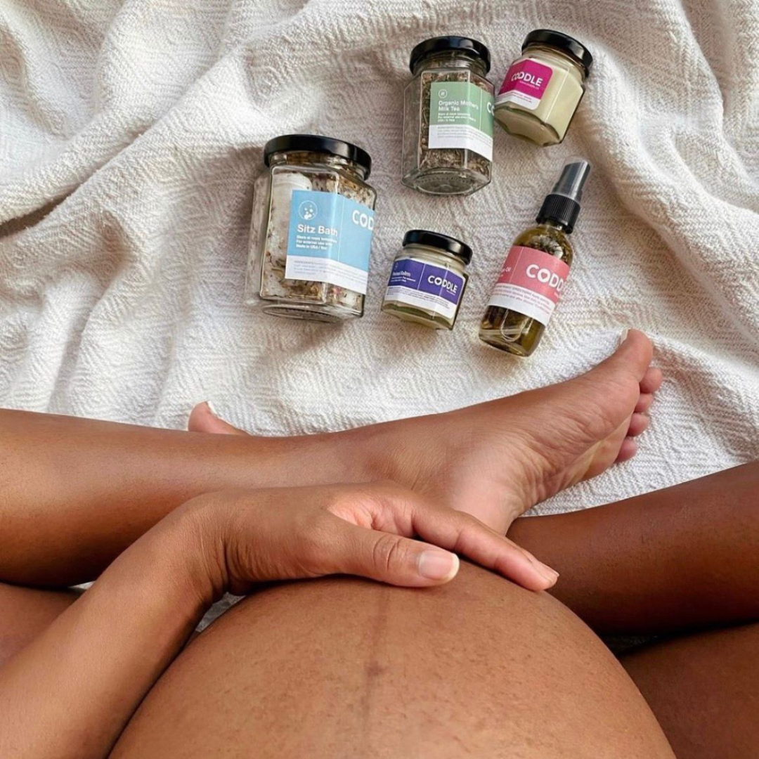 Pregnant mother resting with CODDLE postpartum recovery kit products while preparing for the fourth trimester.