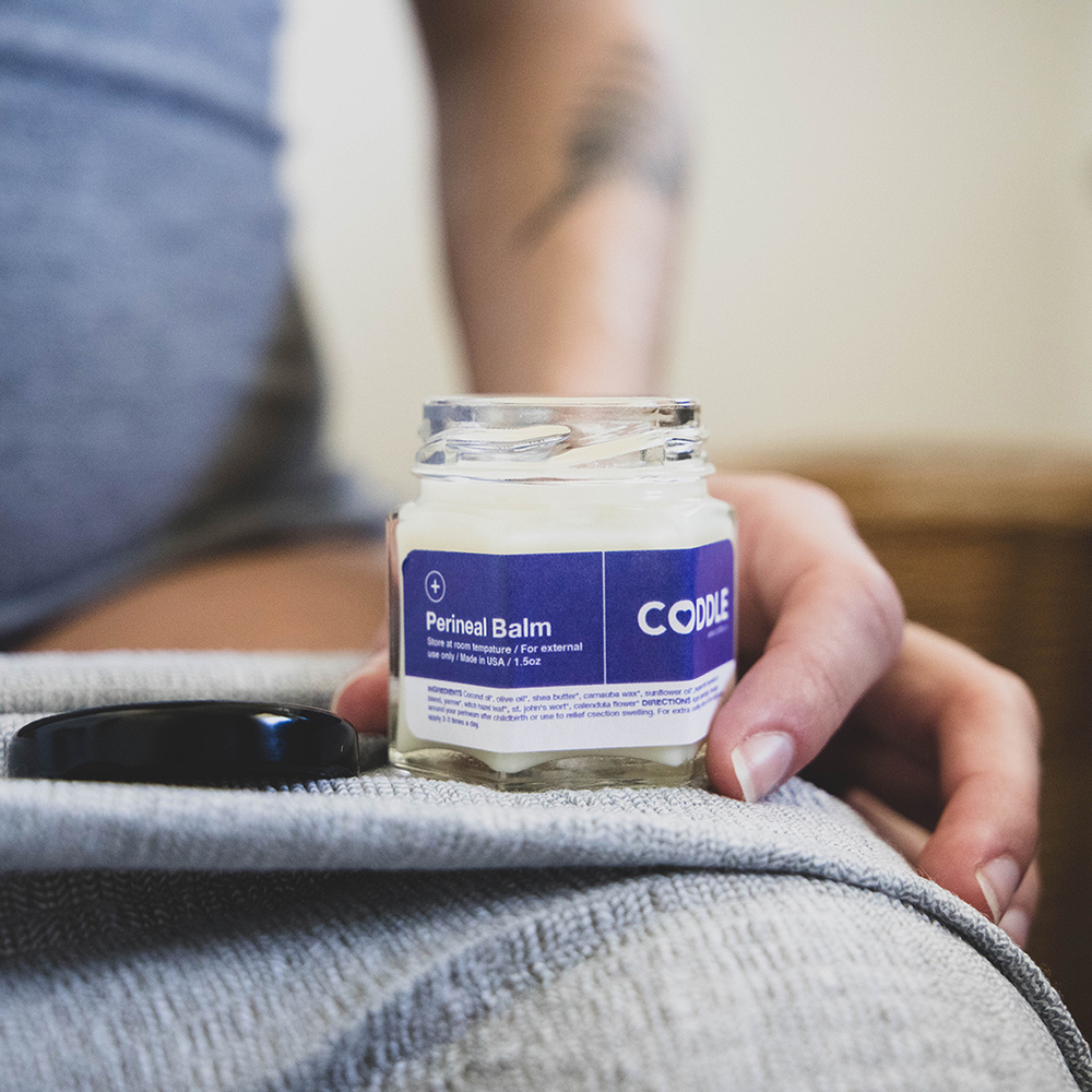Person holding a jar of Perineal Balm with CODDLE branding.