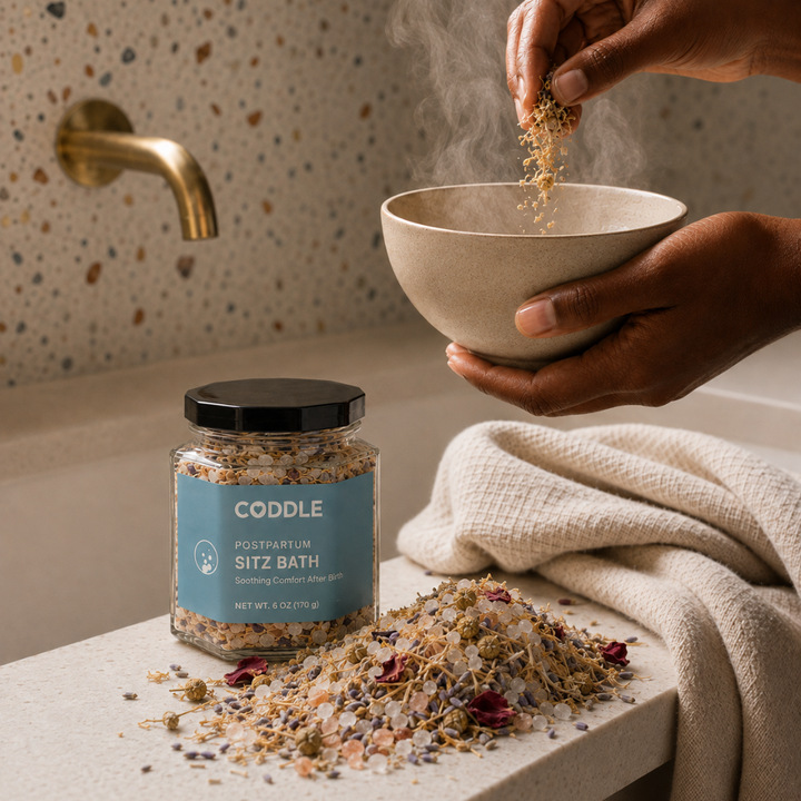 Person preparing a soothing postpartum sitz bath with CODDLE Sitz Bath botanicals in a warm, spa-inspired bathroom.