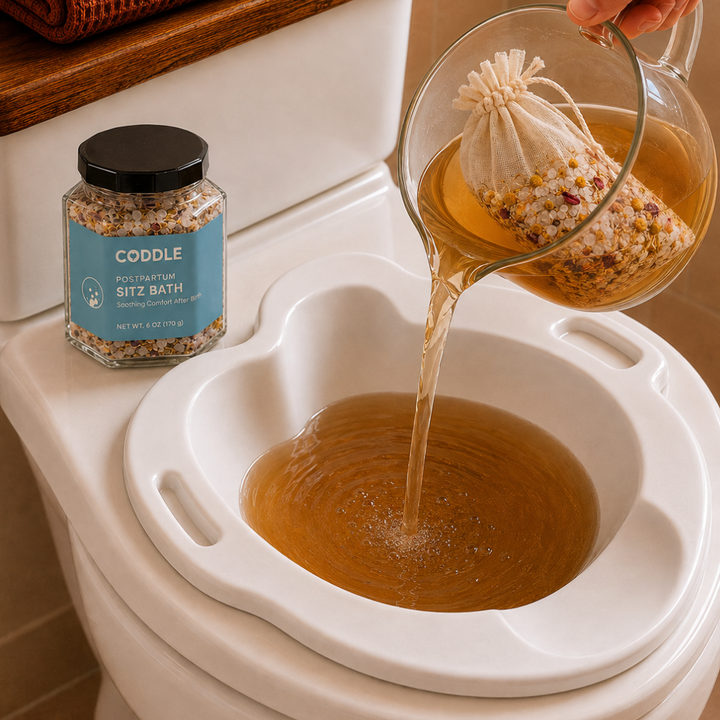 CODDLE Postpartum Sitz Bath botanical infusion being poured from a glass pitcher into a sitz bath basin.