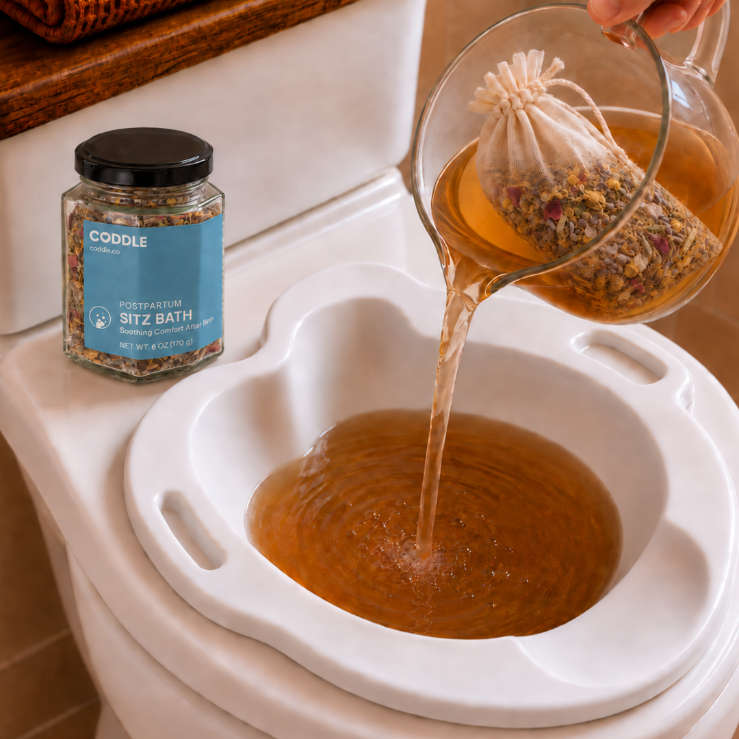 CODDLE Postpartum Sitz Bath botanical infusion being poured from a glass pitcher into a sitz bath basin.
