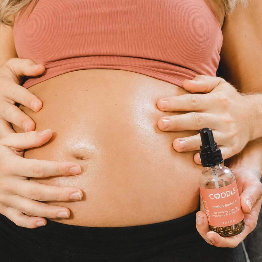Pregnant mother applying CODDLE Bath & Body Oil during a belly massage with partner support, featuring nourishing pregnancy and postpartum body oil in a lifestyle setting.