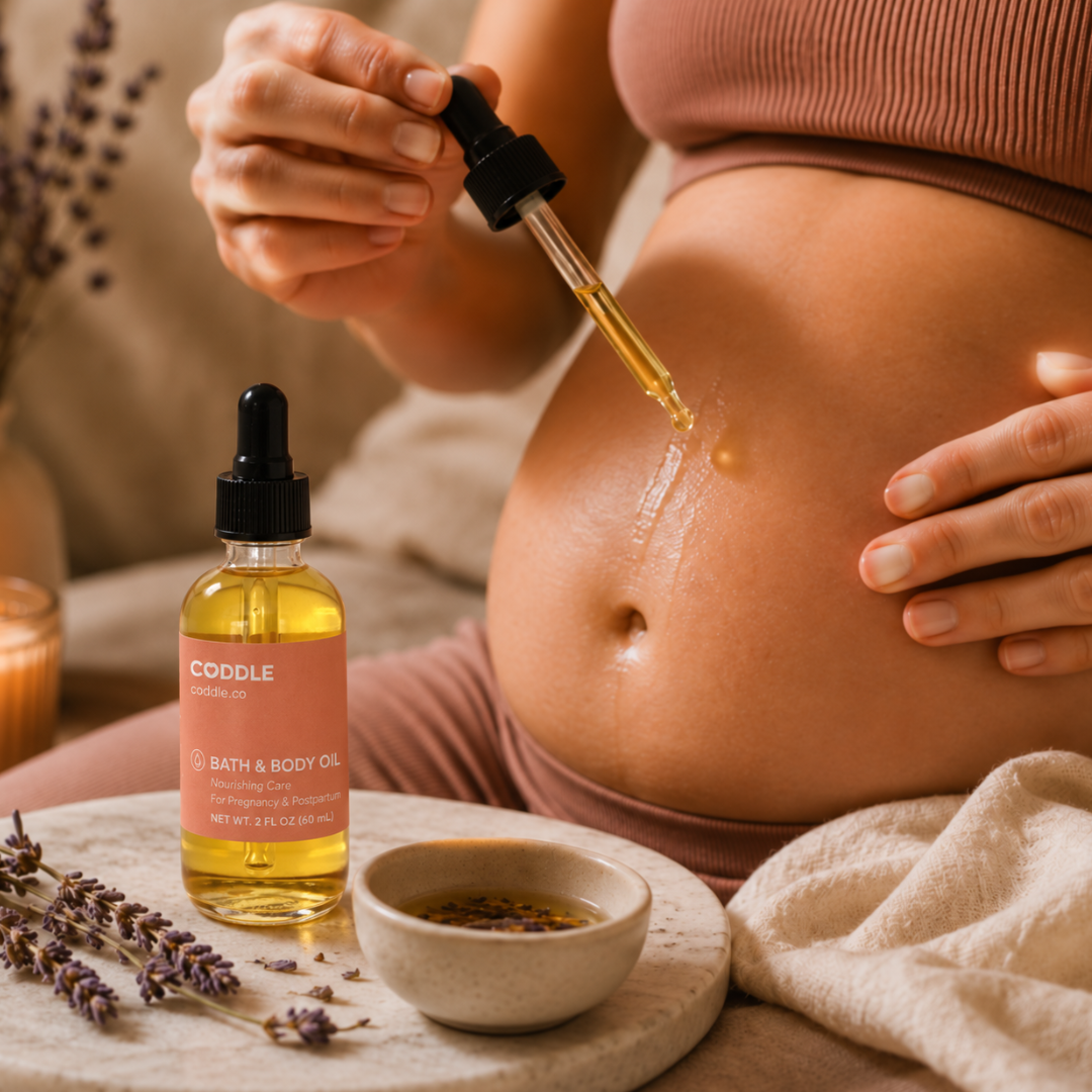 Pregnant mother using CODDLE Bath & Body Oil during a calming self-care ritual, applying nourishing pregnancy and postpartum body oil with a dropper in a warm spa-inspired setting.