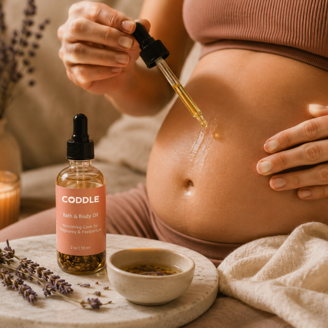 Pregnant mother using CODDLE Bath & Body Oil during a calming self-care ritual, applying nourishing pregnancy and postpartum body oil with a dropper in a warm spa-inspired setting.