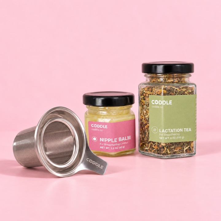 CODDLE Breastfeeding Kit with Lactation Tea, Nipple Balm, and stainless steel tea strainer on a pink background.
