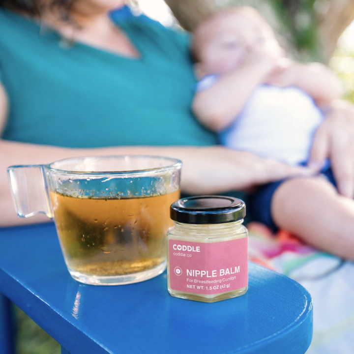 Mother sitting on a blue bench with the CODDLE Lactation Tea and Nipple Balm kit.