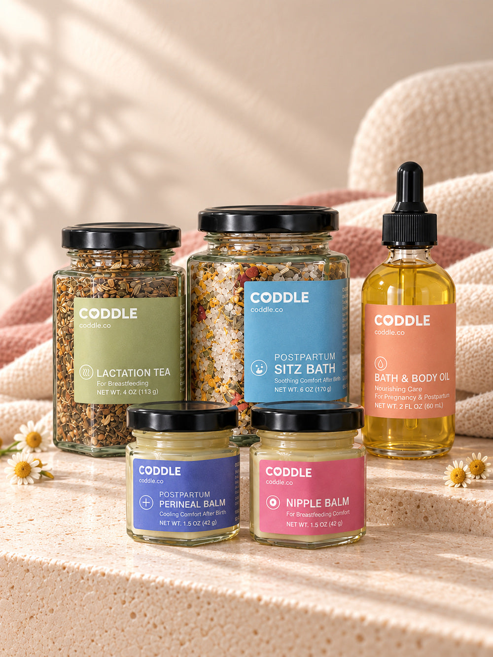 CODDLE postpartum recovery essentials arranged on soft white bedding.