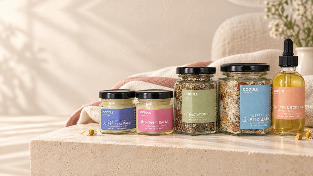 CODDLE postpartum recovery essentials arranged on soft white bedding.