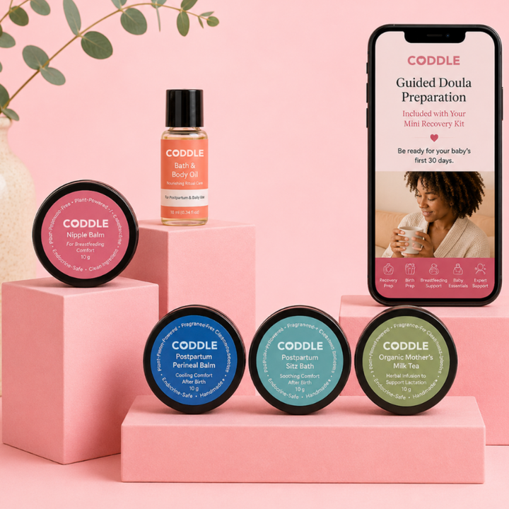 CODDLE Mini Postpartum Recovery Kit featuring Bath & Body Oil, Nipple Balm, Postpartum Perineal Balm, Postpartum Sitz Bath, Organic Mother's Milk Tea, and Guided Doula Preparation on a premium blush display