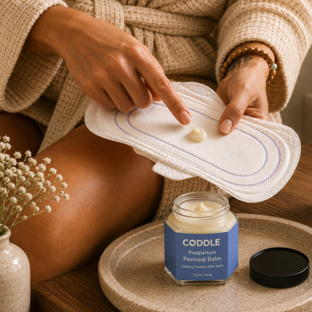 Postpartum mother applying CODDLE Perineal Balm to a pad for cooling comfort after birth.