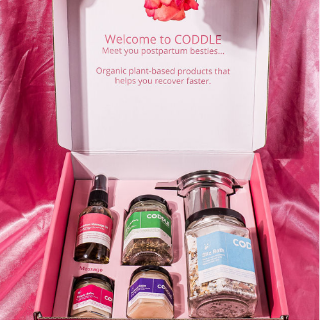 Open CODDLE postpartum care kit with sitz bath, perineal balm, nipple balm, massage oil, and lactation tea.
