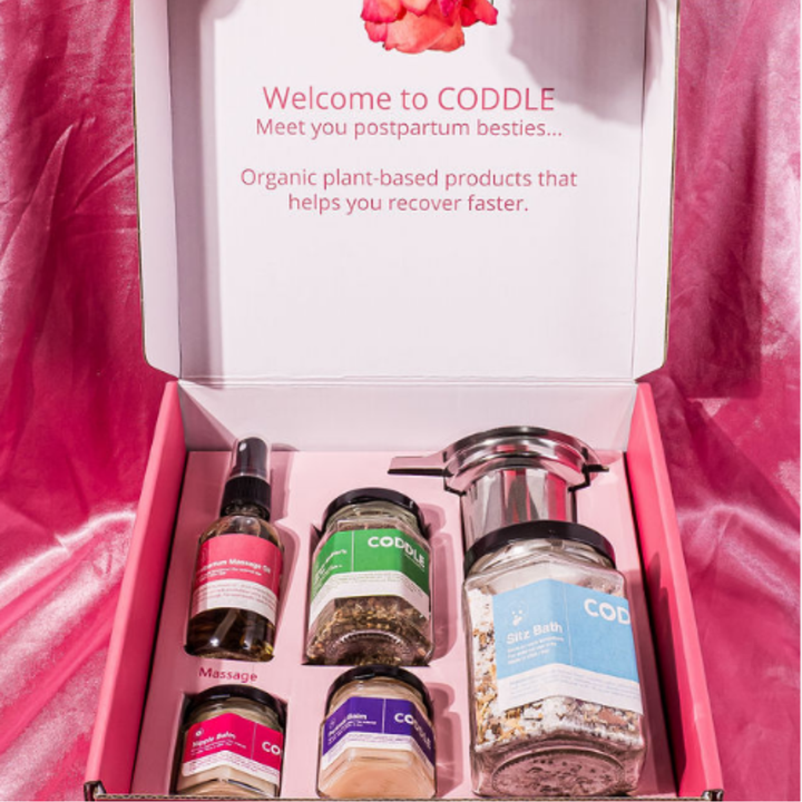 Open CODDLE postpartum care kit with sitz bath, perineal balm, nipple balm, massage oil, and lactation tea.