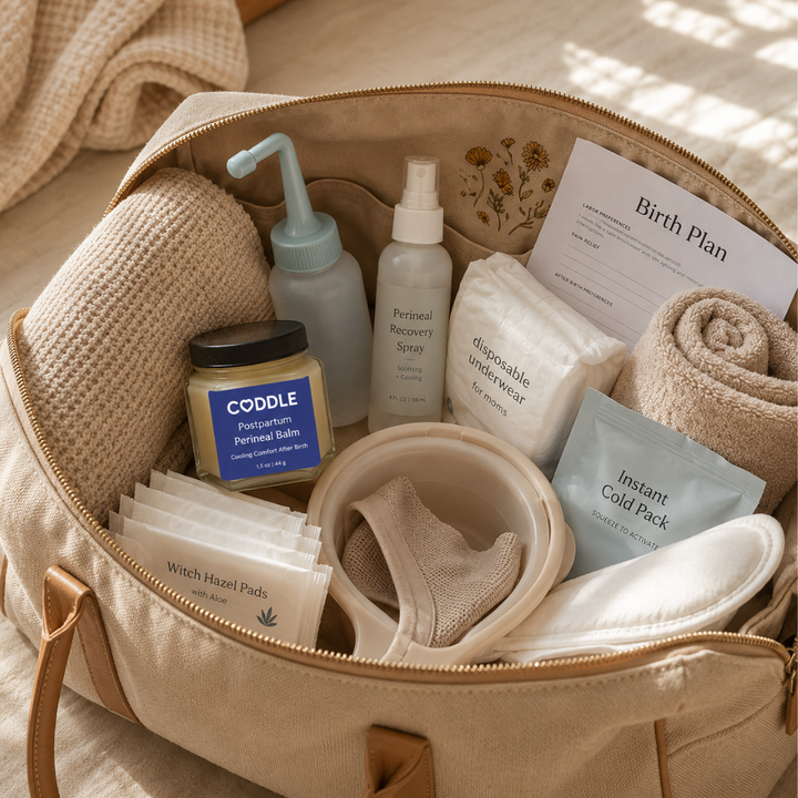 Open hospital bag packed with postpartum recovery essentials featuring CODDLE Postpartum Perineal Balm, a peri bottle, cooling pack, witch hazel pads, disposable underwear, towels, and a birth plan, ready for the first days after birth.