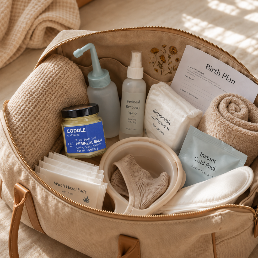Open hospital bag packed with postpartum recovery essentials featuring CODDLE Postpartum Perineal Balm, a peri bottle, cooling pack, witch hazel pads, disposable underwear, towels, and a birth plan, ready for the first days after birth.