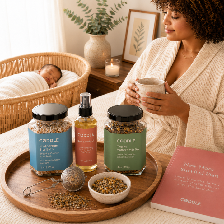 CODDLE Postpartum Recovery Kit featured in a cozy fourth trimester scene with Postpartum Sitz Bath, Organic Mother's Milk Tea, and Body & Bath Oil on a wooden tray beside a new mother enjoying tea while her baby sleeps nearby.