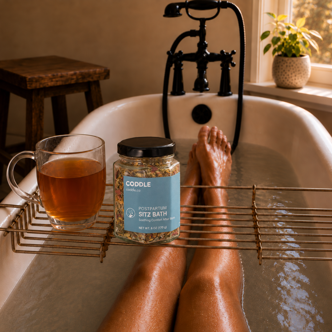 A relaxing postpartum sitz bath with CODDLE Postpartum Sitz Bath herbal blend on a bath caddy beside herbal tea, creating a calming recovery ritual in a warm spa-inspired bathroom.