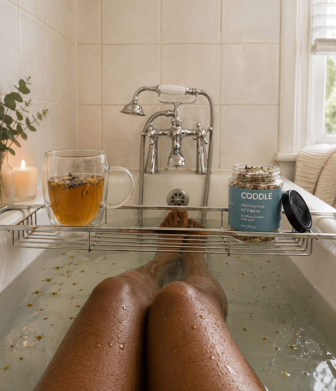 CODDLE Postpartum Sitz Bath featured beside a warm bath and herbal tea, supporting a soothing postpartum recovery soak with botanical ingredients for comfort after birth.