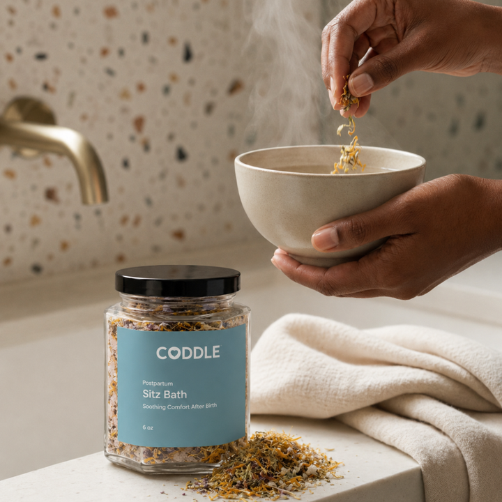 Person preparing a soothing postpartum sitz bath with CODDLE Sitz Bath botanicals in a warm, spa-inspired bathroom.
