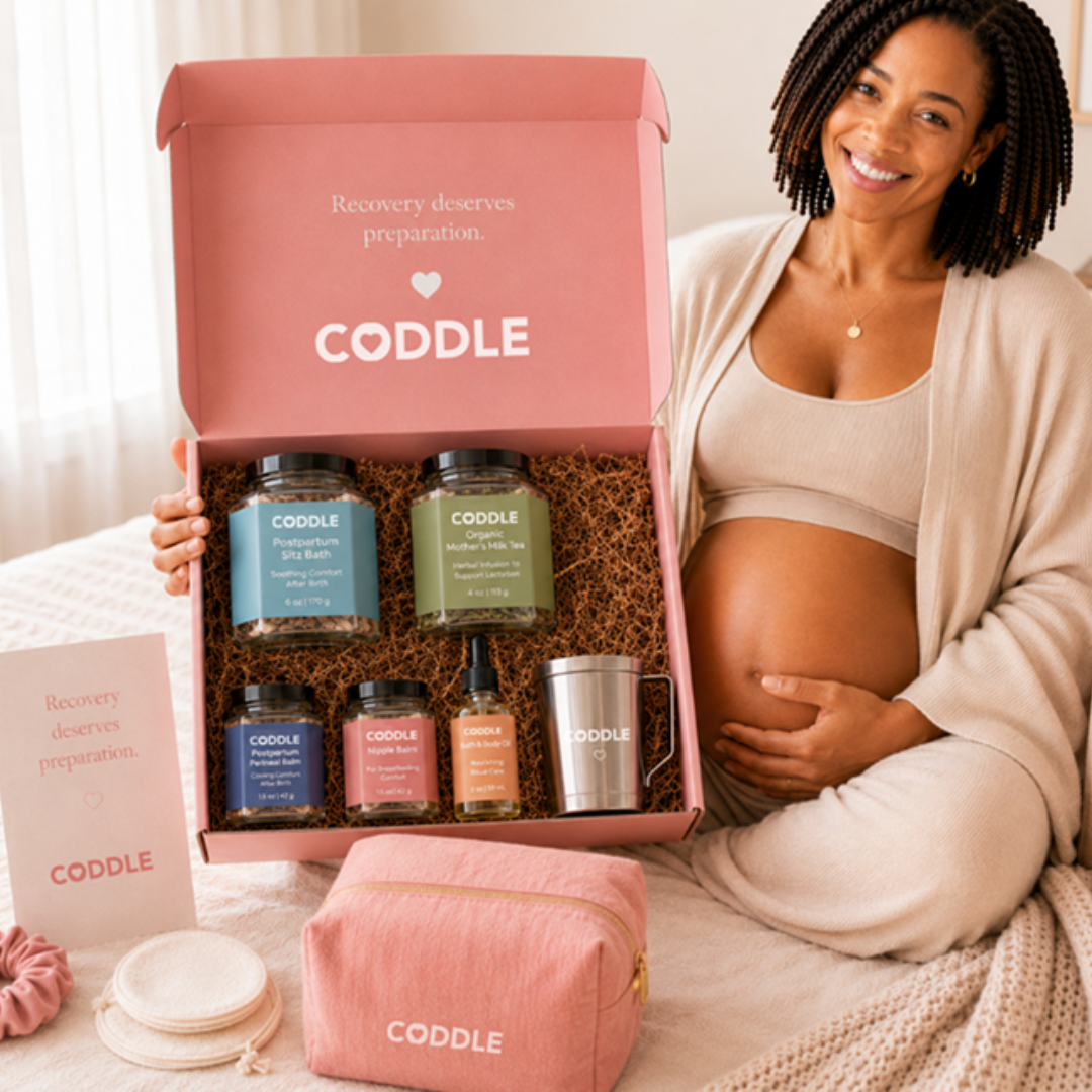 Pregnant woman holding the CODDLE Postpartum Recovery Box featuring Postpartum Sitz Bath, Organic Mother's Milk Tea, Nipple Balm, Postpartum Perineal Balm, Body & Bath Oil, and a stainless steel tea infuser.