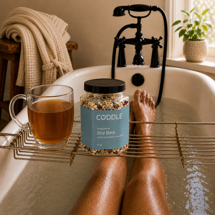 A relaxing postpartum sitz bath with CODDLE Postpartum Sitz Bath herbal blend on a bath caddy beside herbal tea, creating a calming recovery ritual in a warm spa-inspired bathroom.